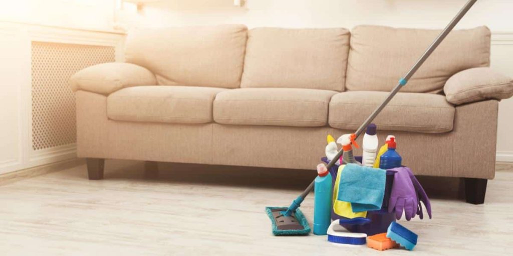 A mop and a bucket of cleaning supplies sitting on the floor in front of a cream-colored sofa.