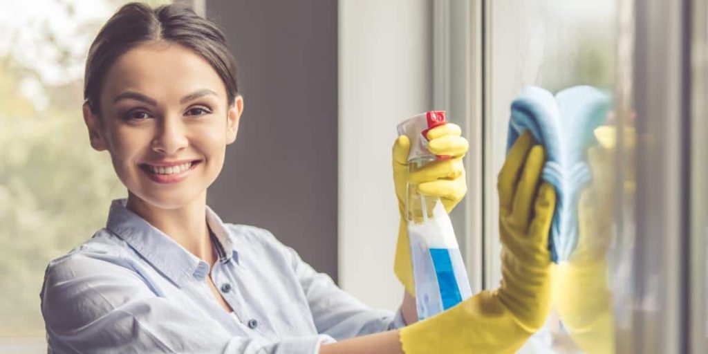 Woman smiling and cleaning a glass windowpane.